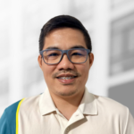 A man with short dark hair, glasses, and braces smiles at the camera. He is wearing a light-colored collared shirt with a blue and yellow accent—ready to help you hire RESTful API developers for your next project.