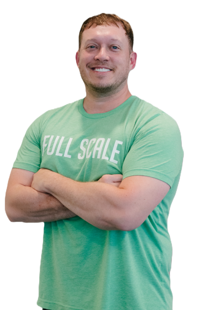 Man wearing a green "Full Scale" t-shirt stands with arms crossed, smiling, against a white background.