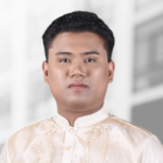 A man with short black hair wearing a cream-colored traditional embroidered shirt stands in front of a blurred background, evoking the professionalism needed to scale projects or manage complex databases.